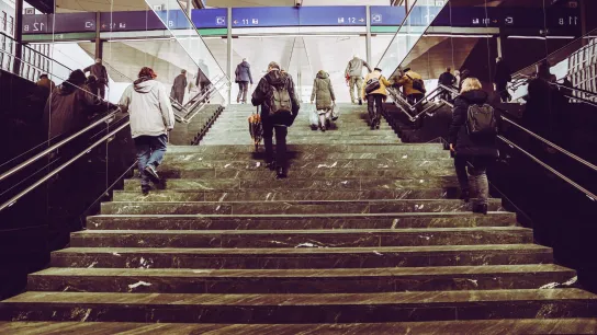 PROMENZ/dragan_dok Mehrere Personen gehen die Stufen in einer Bahnhofshalle hinauf.