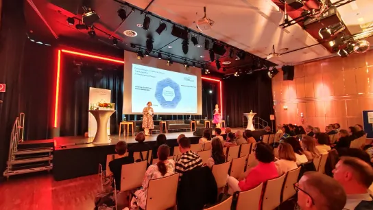 Demenztagung 2024 Eine Person steht am Podium und es sind Zuschauer:innen zu sehen.